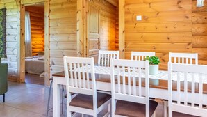 A wooden cabin interior with a dining table and chairs, a small plant, and a cozy fireplace.