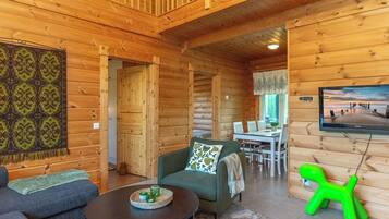 A log cabin interior with a dining area, a television mounted on the wall, and a green plastic chair.