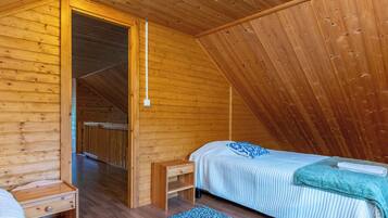 A cozy attic bedroom with a wooden sloped ceiling, a single bed with a blue pillow, a small wooden nightstand, and a blue patterned rug.