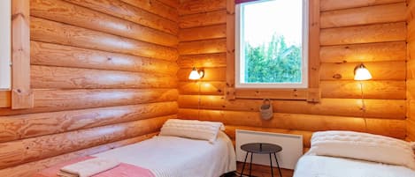Une cabine avec deux lits, une fenêtre donnant sur la forêt et des lampes fixées au mur.