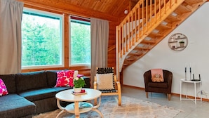 Una sala de estar acogedora con una escalera de madera, un sofá, una mesa redonda de centro y vistas al exterior.