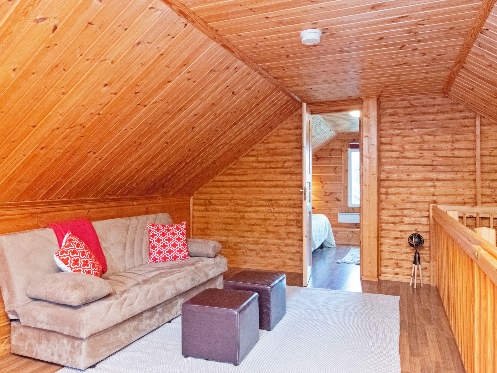 Une chambre mansardée chaleureuse avec un plafond en pente en bois, un canapé avec des coussins, une petite table et une vue sur une pièce adjacente.