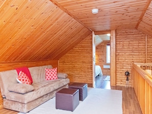 Un dormitorio estilo loft acogedor con techo inclinado de madera, un sofá con cojines, una mesita y vista a una habitación contigua.