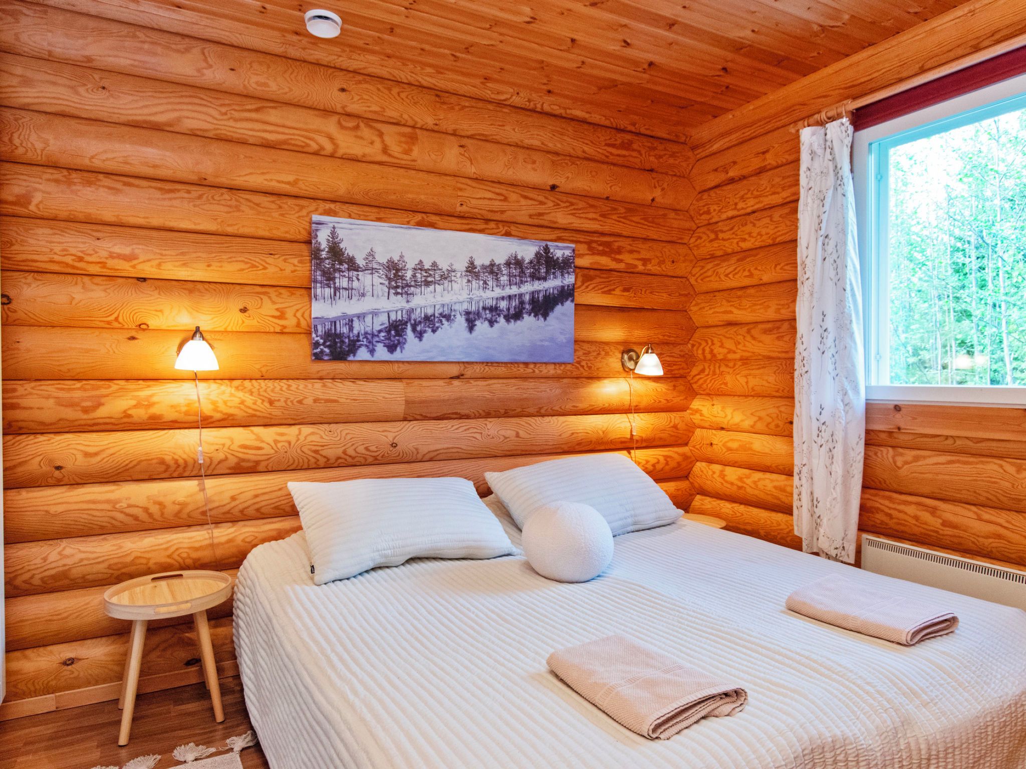 Une chambre dans un chalet en bois, avec un lit, deux lampes de chevet, une petite table et une fenêtre avec des rideaux.