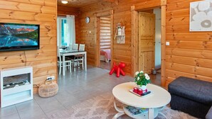 Interior acogedor de una cabaña con comedor, televisor montado en la pared, una mesita con planta y sofá.