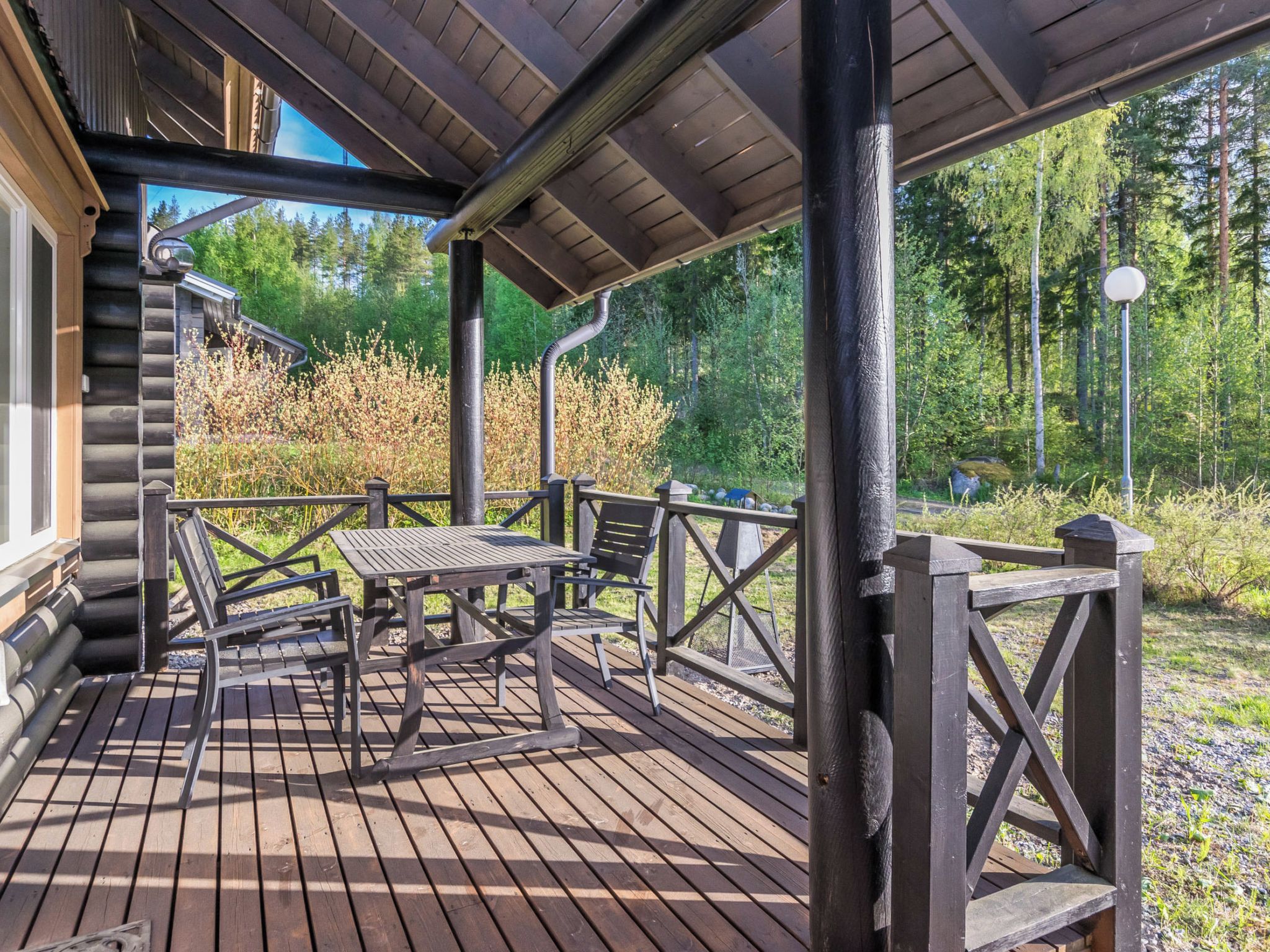 Eine Holzterrasse mit Tisch und Stühlen, umgeben von bewaldetem Gelände.