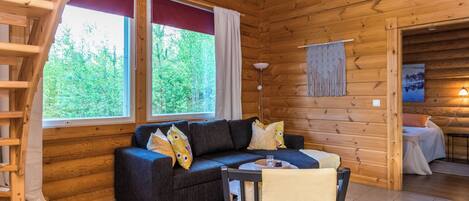 Ein gemütliches Blockhaushaus-Interieur mit einer Couch, einem Sessel, einem Tisch und einer Treppe.