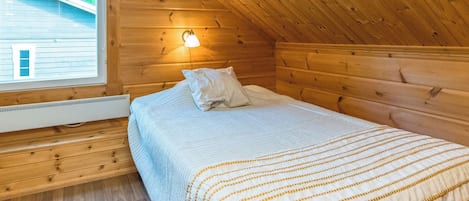 Een enkel bed in een blokhut met een schuine kap en een vluchtrouteborden boven de deur.