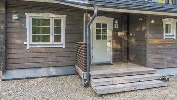 A wooden cabin with a front porch, a door, and two windows.