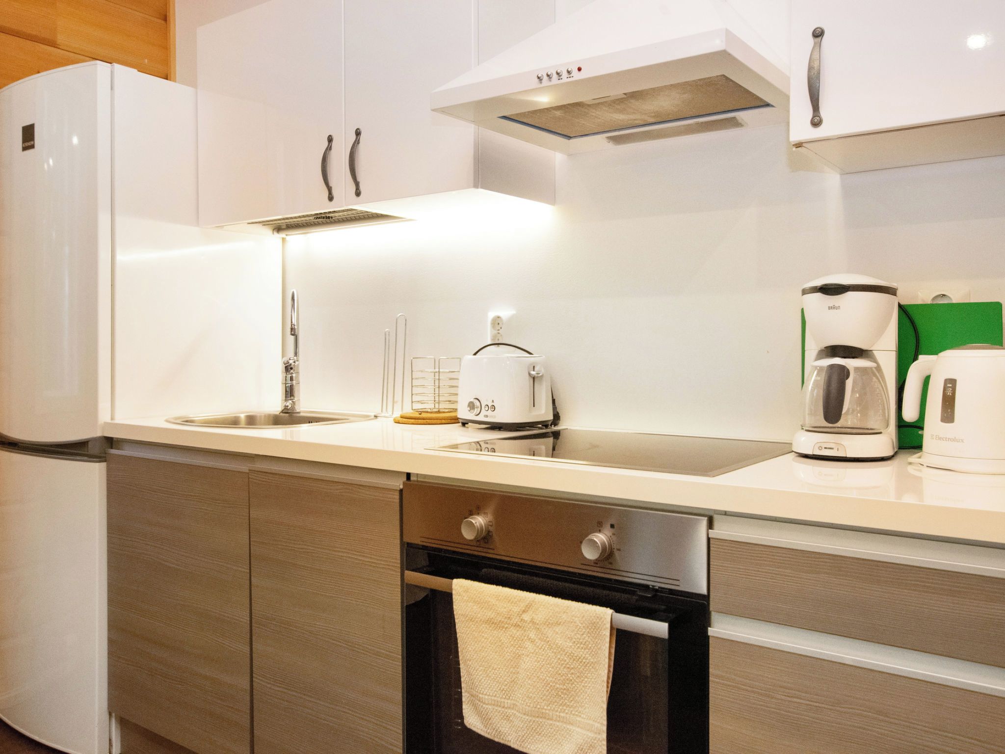 A modern kitchen with white cabinetry, a stainless steel sink, a coffee maker, and a kettle.
