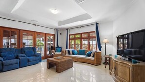 Ein geräumiges Wohnzimmer mit einem blauen Sofa, einem Rattansofa, einem Couchtisch und einem Fernseher auf einer Holzkassette.