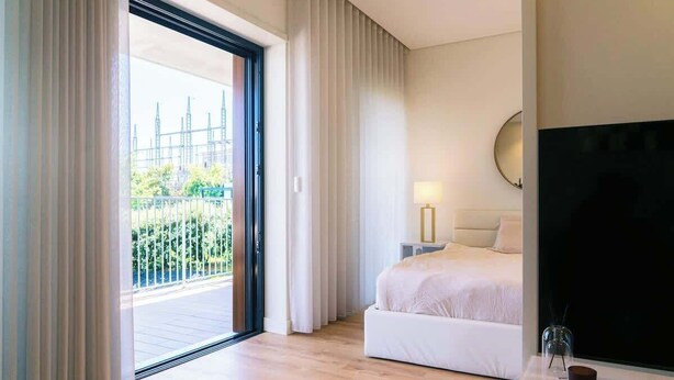 A modern hotel room with a large bed, a TV, and a balcony with a city view.