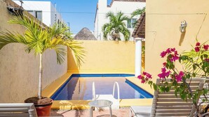 Piscina com cadeira e banco, cercada por um muro amarelo e uma palmeira.