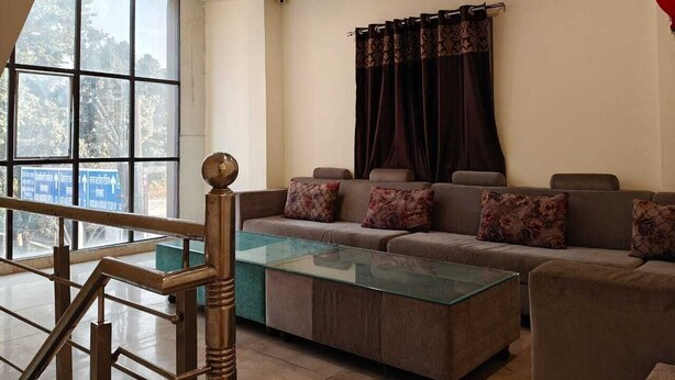 Un salón con un conjunto de sofás, una mesa de centro de cristal, una escalera con barandilla y un ventanal con cortinas.