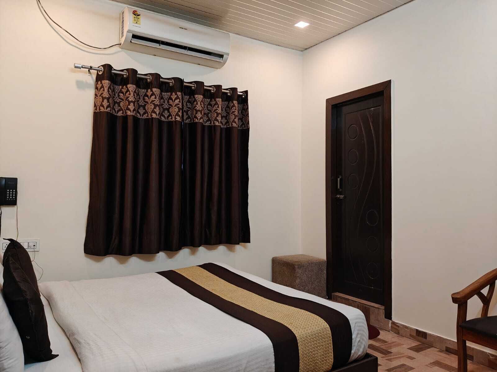 A hotel room with a bed, a chair, an air conditioning unit, a telephone, and a door.