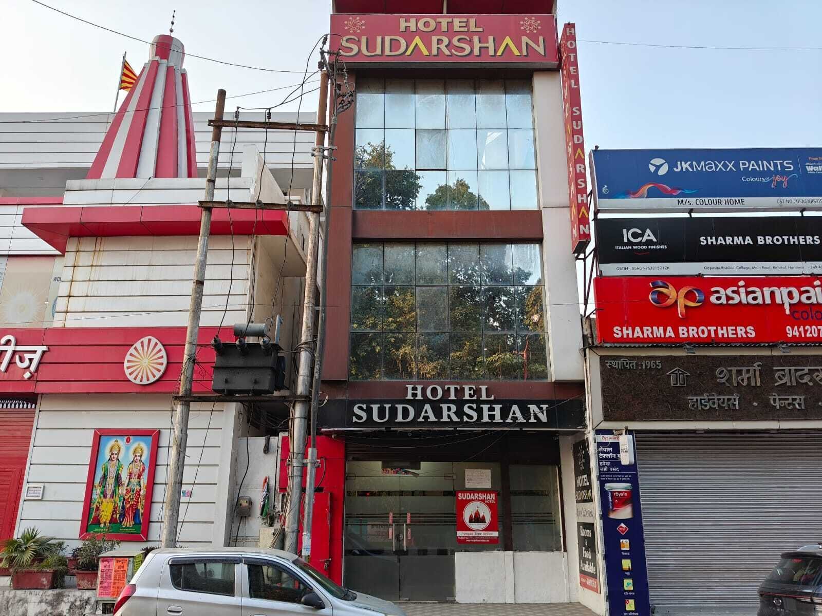 A hotel named 'Hotel Sudarshan' with a prominent sign, a red and white facade, and a large window display.