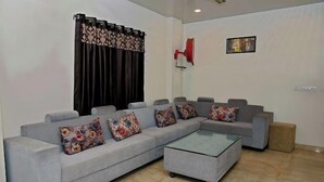 Una sala de estar con un sofá seccional gris, una mesa de centro de vidrio y un altavoz rojo montado en la pared.