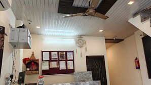 Zona de recepción con mostrador de mármol, ventilador de techo, reloj y un tablón de anuncios con varios avisos.
