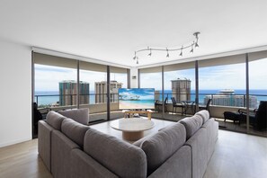 A modern living room with a large TV, comfortable seating, and a balcony with a city view. - Penthouse Level - Stunning Diamond Head & Waikiki Beach Views - Free Parking! (Honolulu)