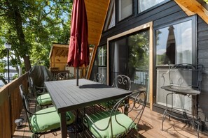 Eine Holzterrasse mit Tisch und Stühlen, einem roten Sonnenschirm und einem Metallstuhl mit Netzrücklehne.