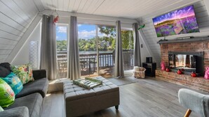 A cozy living room with a fireplace, a large TV, and a view of a lake.
