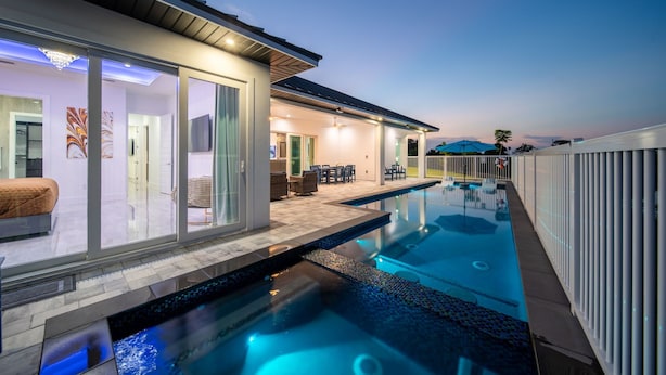 A modern house with a swimming pool, glass doors leading to a patio, and a view of the sky.