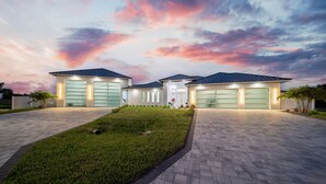 A modern two-story house with three garage doors, a well-maintained lawn, and a paved driveway.