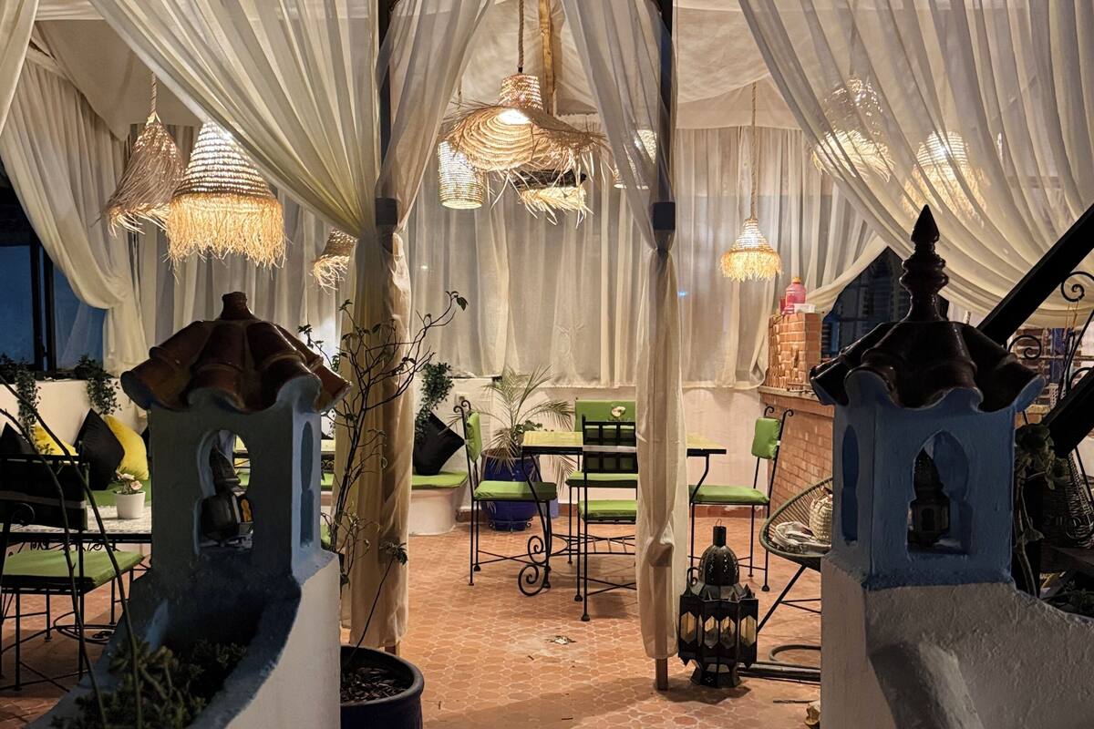 A covered outdoor seating area with white drapes, wicker lamps, and green chairs.