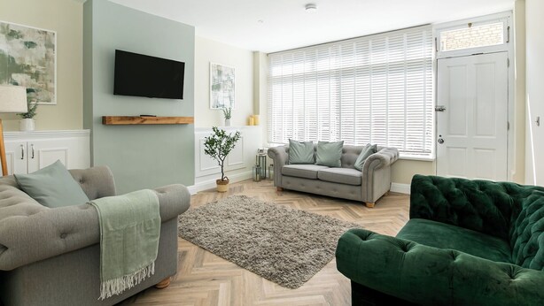 Una sala moderna con un sofá gris, un sillón verde y un juego de sofás gris.