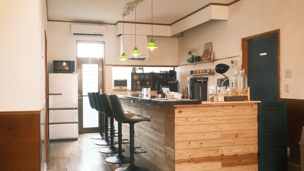 A kitchen with a wooden bar counter, bar stools, a coffee machine, and hanging pendant lights. - Guest House SAKURAZUKISOU - Hostel (Kagoshima)