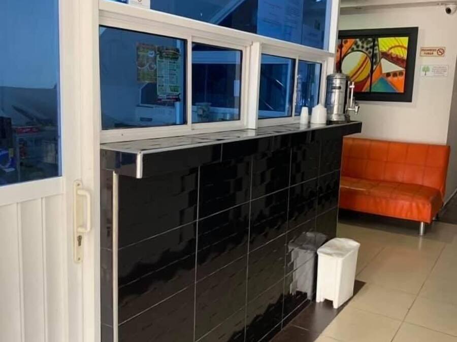 Un área de recepción con una pared de baldosas negras, un ventanal azul y un taburete blanco pequeño.