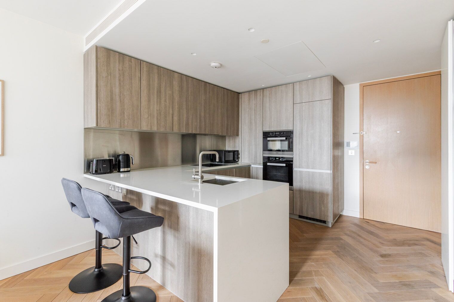 Une cuisine moderne dotée d’un îlot central, de tabourets de bar, d’appareils électroménagers en acier inoxydable et de meubles de rangement en bois.