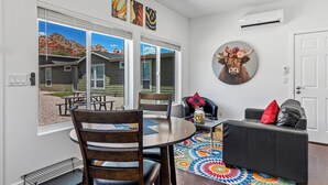 A dining area with a round table and chairs, a black leather sofa, and a colorful rug. - Chimney Rock Suite - Unit C - Red Rock Retreat (Sedona)