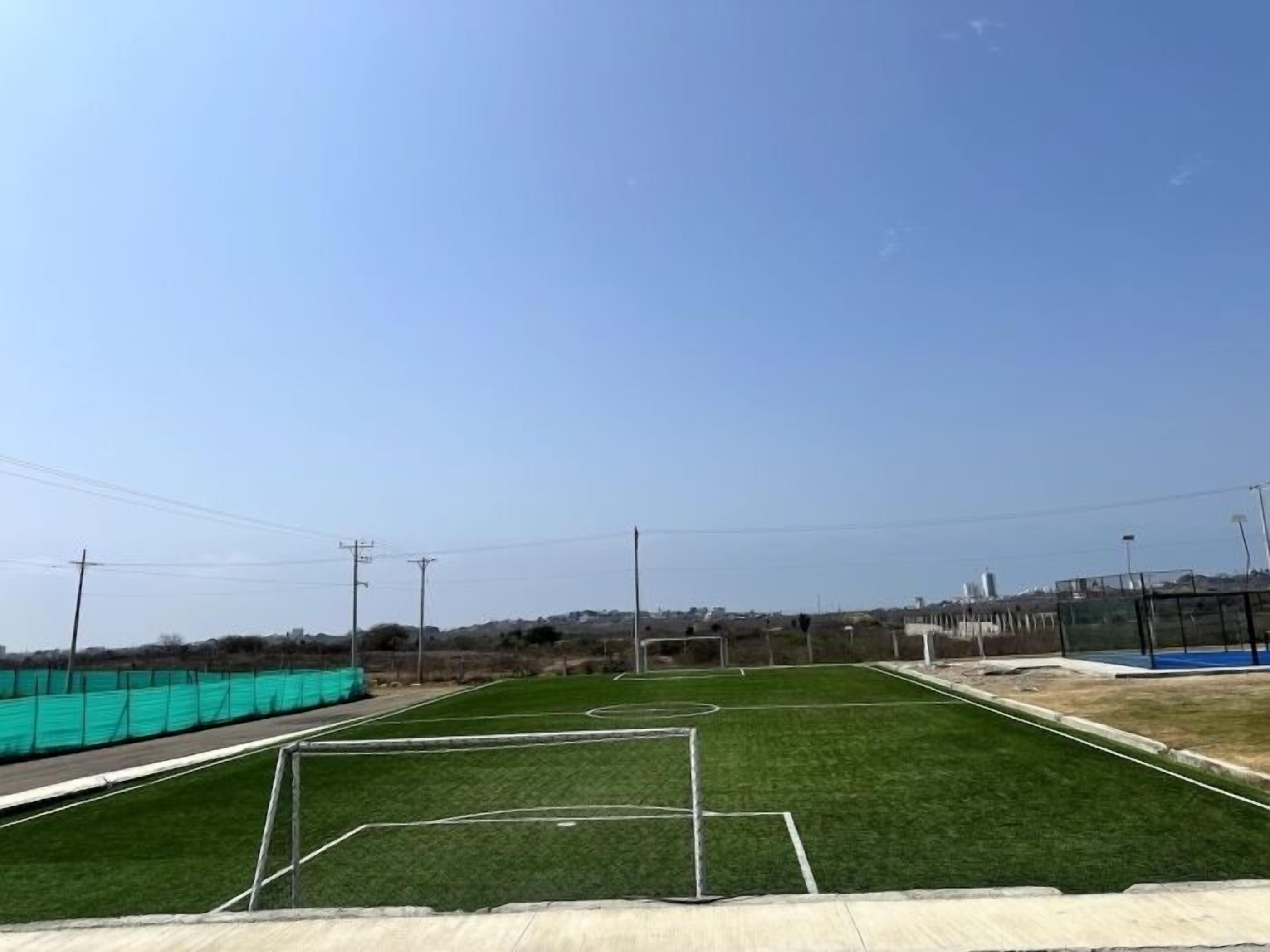 Un terrain de football avec des poteaux de but, entouré d’une clôture et bordé de poteaux électriques.