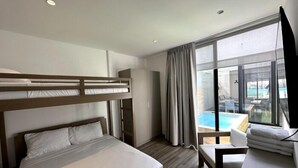 Habitación de hotel con literas, un escritorio con silla, un ventanal con cortinas y vista a una piscina.