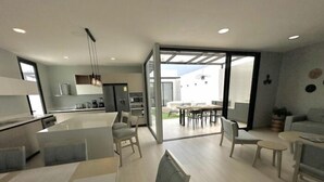 A modern open-plan living area with a kitchen, dining space, and a large sliding glass door leading to an outdoor patio.