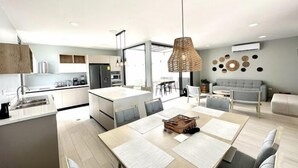 Une cuisine moderne dotée d’un îlot central, d’un coin repas avec une table et des chaises, et d’un espace de vie avec un canapé et des œuvres d’art décoratives au mur.