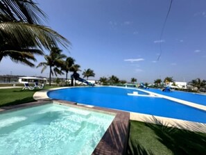 Une piscine avec un toboggan, entourée de palmiers et de chaises longues.