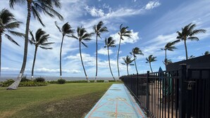Un sentier bordé de palmiers et d’une clôture, avec une piste d’athlétisme bleue et orange de chaque côté, qui mène à un plan d’eau.