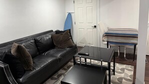 Una sala de estar moderna con un sofá de cuero negro, una mesa de centro de vidrio y una mesa de comedor con mantel a rayas.