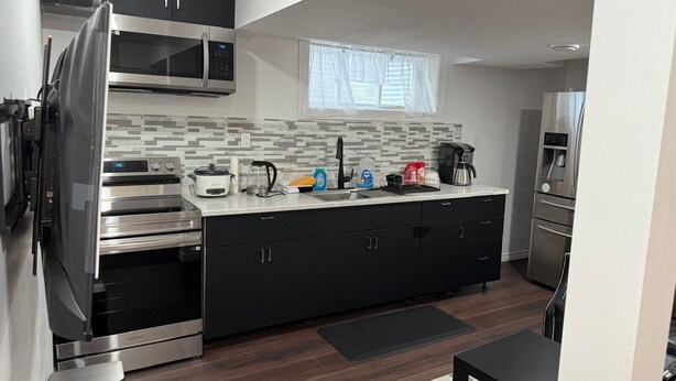 Una cocina moderna con electrodomésticos de acero inoxidable, microondas, cafetera y lavamanos.