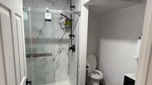 Un baño moderno con ducha de vidrio, inodoro y una pequeña zona de lavamanos.