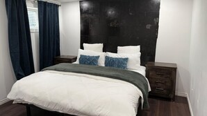 Un dormitorio moderno con una cama grande, cabecera de madera oscura y una ventana con cortinas azules.