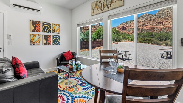 Una sala de estar con sofá, mesa de centro y sillas, un tapete colorido y un ventanal con vistas panorámicas.