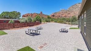 Un patio de grava con mesas de picnic, una valla de madera y un edificio con ventanas.