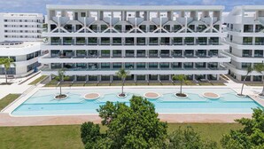 A modern multi-story hotel with a central pool area, surrounded by greenery and palm trees.