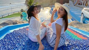 Two people sitting on a blue mosaic floor by the sea with a view of the ocean and a building in the background. - OSANNA BEACH RESORT (Gunturharjo)