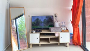 A room with a TV on a wooden TV stand, a mirror, and a window with orange curtains. - OSANNA BEACH RESORT (Gunturharjo)