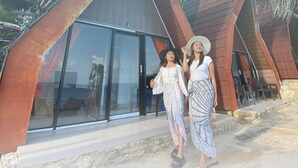 Two people standing in front of a building with large glass windows and a stone base. - OSANNA BEACH RESORT (Gunturharjo)