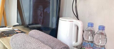 A hotel room with a TV, a coffee maker, two water bottles, a tray with a toothbrush, toothpaste, and a box of Tong Tong Jasmine Tea.